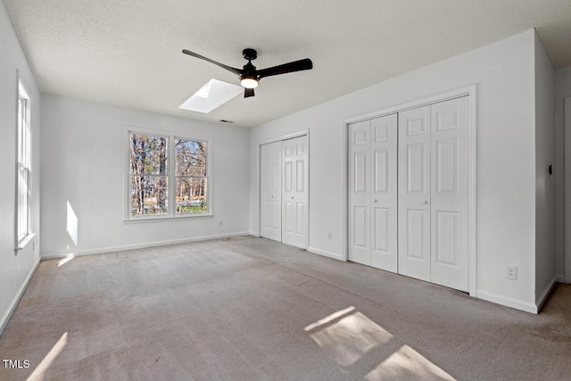 unfurnished bedroom with two closets, baseboards, carpet, a skylight, and a textured ceiling