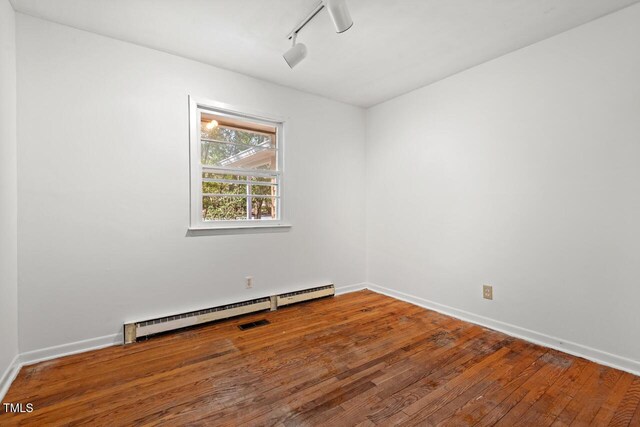 unfurnished room with visible vents, track lighting, a baseboard heating unit, hardwood / wood-style floors, and baseboards