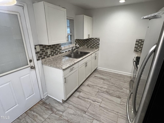 kitchen with backsplash, light stone counters, sink, white cabinetry, and fridge