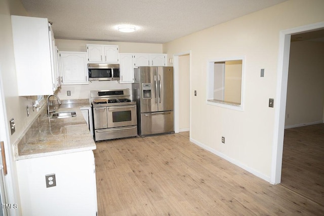 kitchen featuring sink, a textured ceiling, appliances with stainless steel finishes, light hardwood / wood-style floors, and white cabinetry