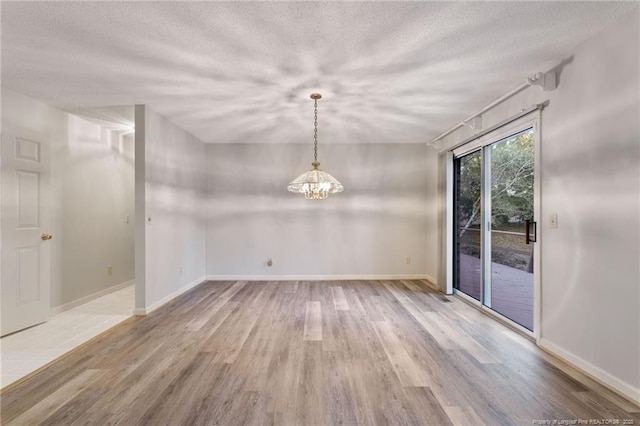 unfurnished dining area with wood-type flooring, a textured ceiling, and an inviting chandelier