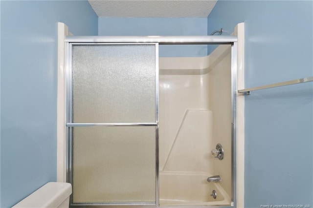 bathroom featuring shower / bath combination with glass door, a textured ceiling, and toilet