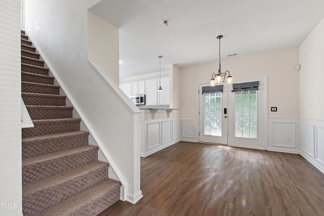 stairs with a chandelier, a decorative wall, wood finished floors, and a wainscoted wall