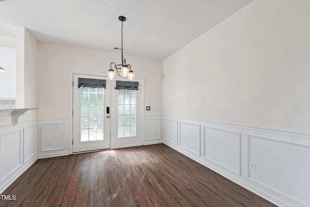 unfurnished dining area featuring a chandelier, wainscoting, a decorative wall, and dark wood-type flooring