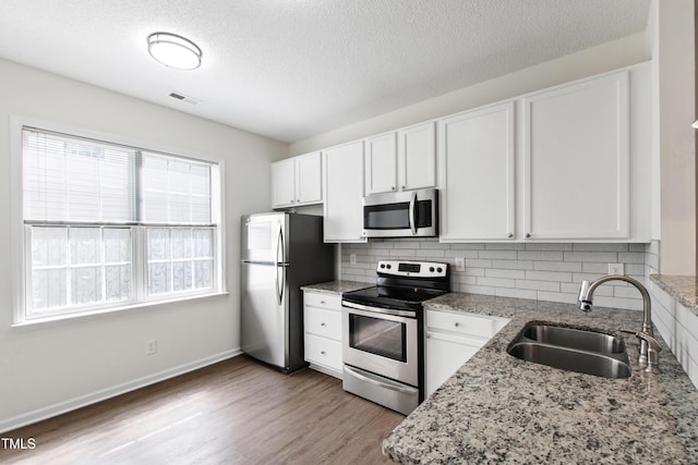 kitchen featuring appliances with stainless steel finishes, a sink, tasteful backsplash, white cabinetry, and light wood finished floors