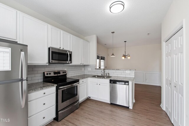kitchen with appliances with stainless steel finishes, a peninsula, a sink, white cabinets, and a wainscoted wall