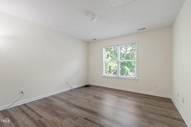 unfurnished room featuring attic access, wood finished floors, and baseboards
