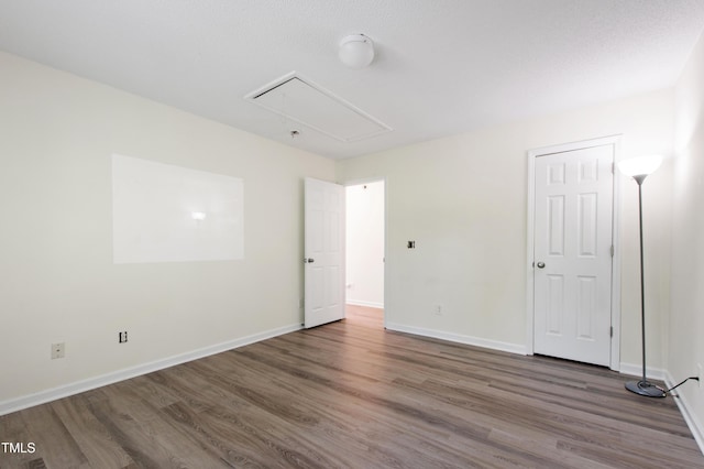 empty room with attic access, wood finished floors, and baseboards