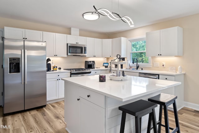 kitchen featuring white cabinets, stainless steel appliances, hanging light fixtures, and a center island with sink