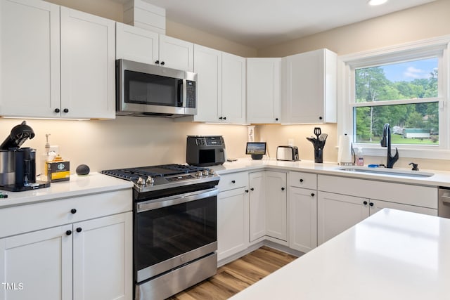 kitchen with sink, white cabinets, stainless steel appliances, and light hardwood / wood-style floors