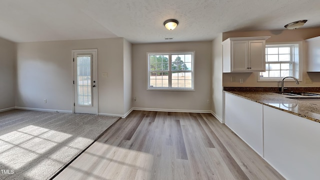 kitchen featuring sink, dark stone countertops, light hardwood / wood-style floors, a textured ceiling, and white cabinets