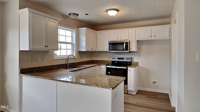 kitchen with sink, dark stone countertops, white cabinetry, kitchen peninsula, and stainless steel appliances