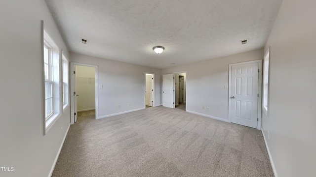 unfurnished bedroom featuring a textured ceiling, light carpet, and multiple windows