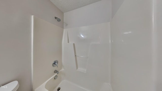 bathroom with a textured ceiling,  shower combination, and toilet