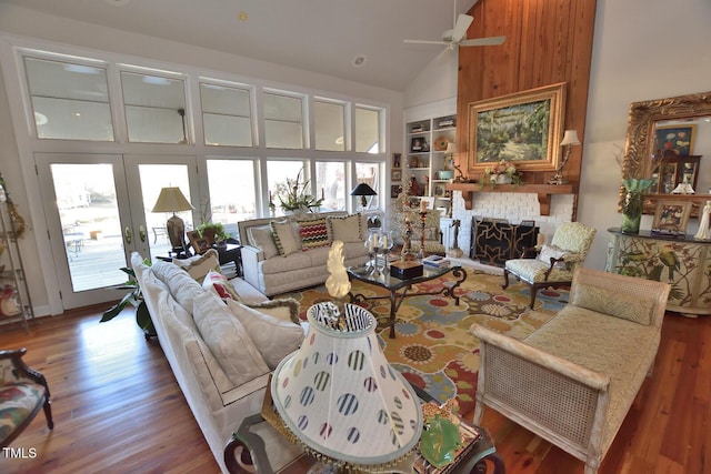 living room featuring ceiling fan, built in features, high vaulted ceiling, hardwood / wood-style floors, and a fireplace