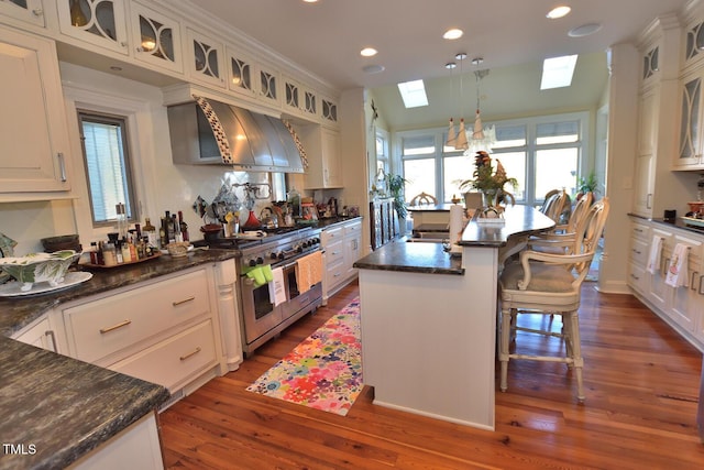 kitchen with double oven range, exhaust hood, a skylight, plenty of natural light, and white cabinetry