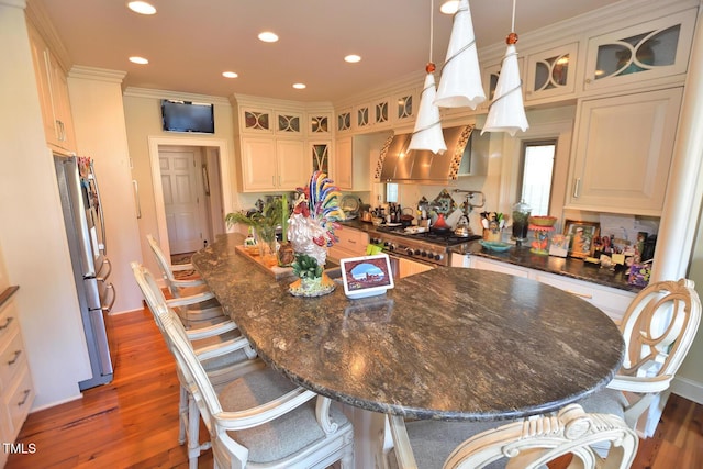 kitchen with hanging light fixtures, dark wood-type flooring, dark stone countertops, stainless steel fridge, and a breakfast bar