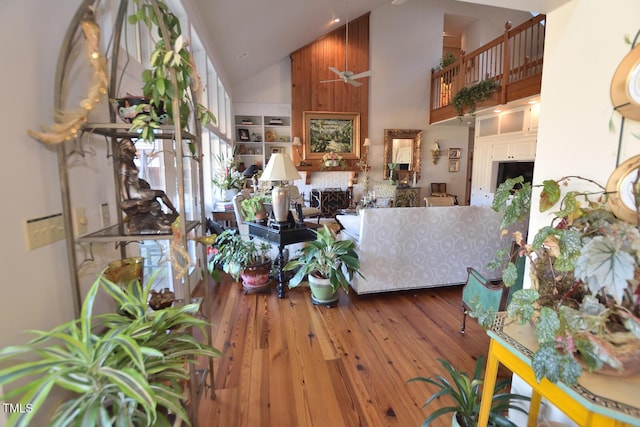 living room with built in shelves, ceiling fan, hardwood / wood-style floors, and high vaulted ceiling