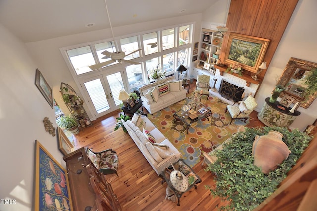 living room featuring ceiling fan, french doors, a high ceiling, a fireplace, and hardwood / wood-style flooring