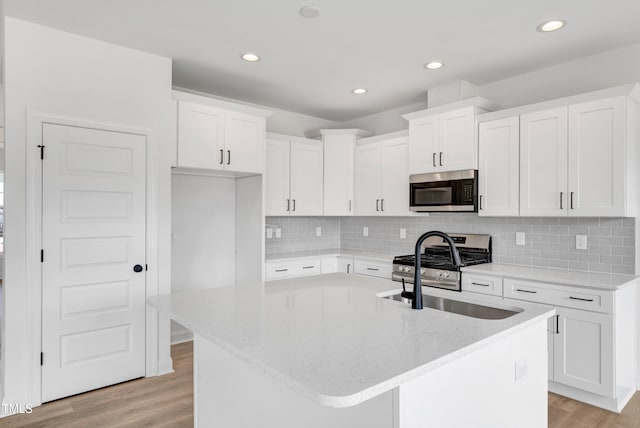 kitchen featuring stainless steel appliances, light wood-style flooring, a sink, a kitchen island with sink, and recessed lighting