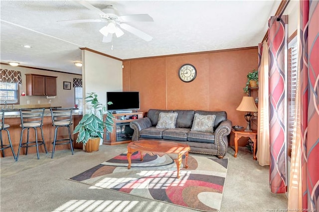 living area with ornamental molding, a ceiling fan, and light colored carpet