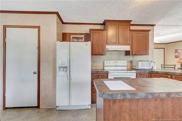 kitchen featuring dark countertops, ornamental molding, brown cabinetry, white appliances, and under cabinet range hood