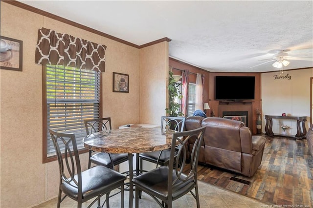 dining area featuring ornamental molding, plenty of natural light, a lit fireplace, and ceiling fan