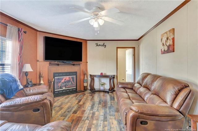 living area featuring a textured ceiling, ceiling fan, a tile fireplace, wood finished floors, and crown molding