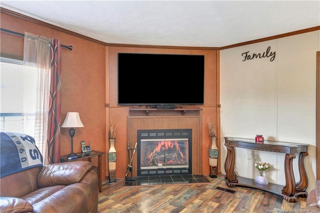 living area with a glass covered fireplace, visible vents, crown molding, and wood finished floors