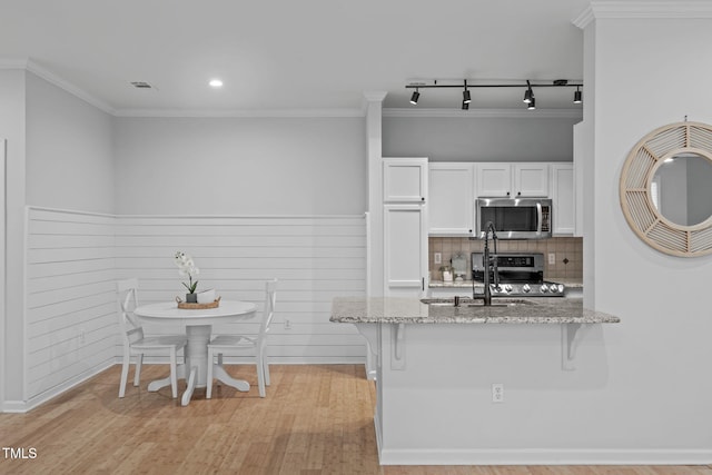 kitchen with stainless steel appliances, a breakfast bar area, white cabinetry, and light stone countertops