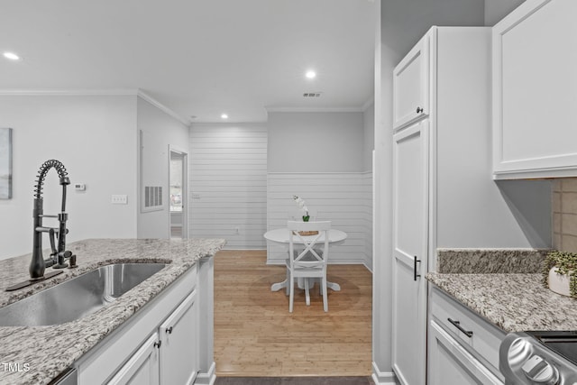 kitchen featuring light stone counters, a sink, visible vents, white cabinets, and light wood-type flooring