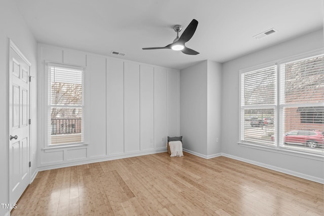 spare room featuring light wood finished floors, visible vents, a decorative wall, and a wealth of natural light