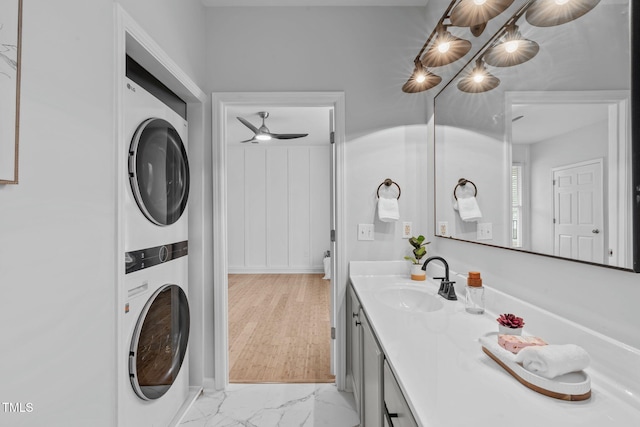 clothes washing area with marble finish floor, stacked washer / dryer, and a sink