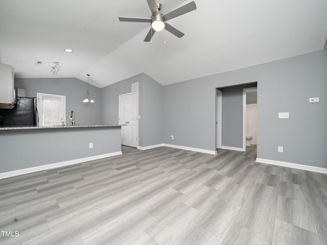 unfurnished living room with light wood-type flooring, ceiling fan with notable chandelier, vaulted ceiling, and sink