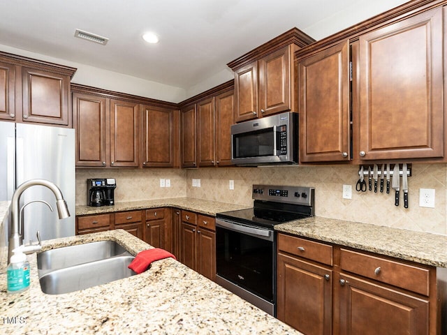 kitchen with light stone countertops, appliances with stainless steel finishes, decorative backsplash, and sink