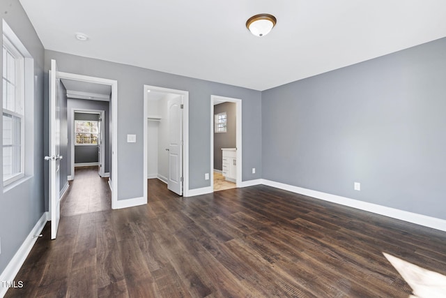 unfurnished bedroom with connected bathroom, a walk in closet, a closet, and dark hardwood / wood-style flooring