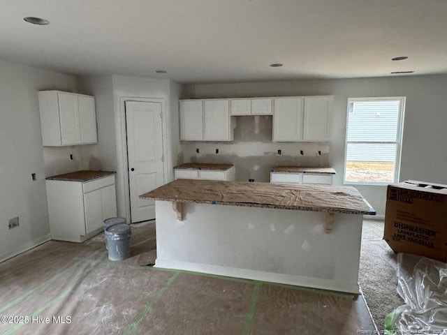 kitchen featuring stone countertops, a breakfast bar, white cabinets, and a kitchen island