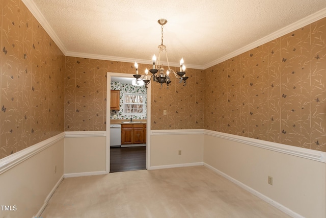 carpeted spare room with a textured ceiling, an inviting chandelier, ornamental molding, and sink