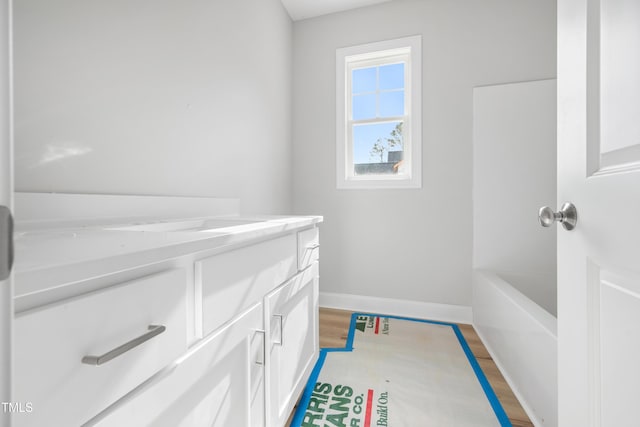 full bathroom featuring baseboards, wood finished floors, vanity, and a bathing tub