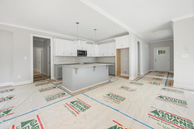 kitchen with white cabinets, a center island, stainless steel microwave, tasteful backsplash, and a breakfast bar