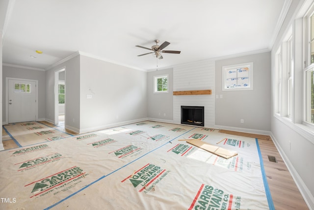 unfurnished living room with a large fireplace, ornamental molding, baseboards, and ceiling fan