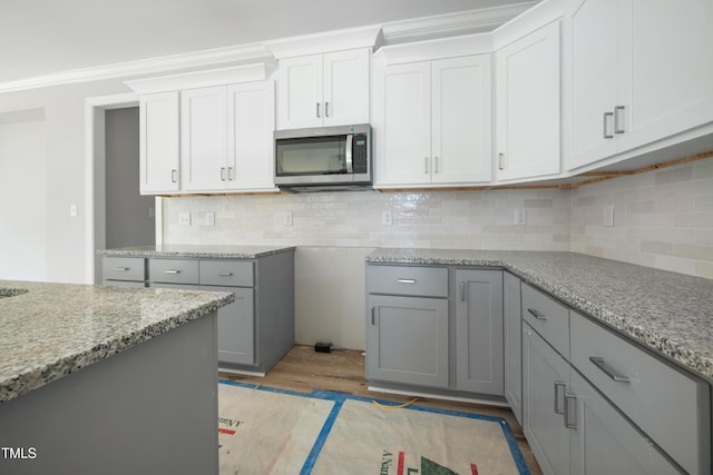 kitchen with stainless steel microwave, light wood-style floors, light stone countertops, and gray cabinetry