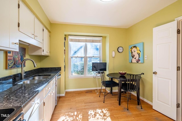 kitchen featuring sink, white cabinets, dark stone countertops, light hardwood / wood-style flooring, and stainless steel dishwasher