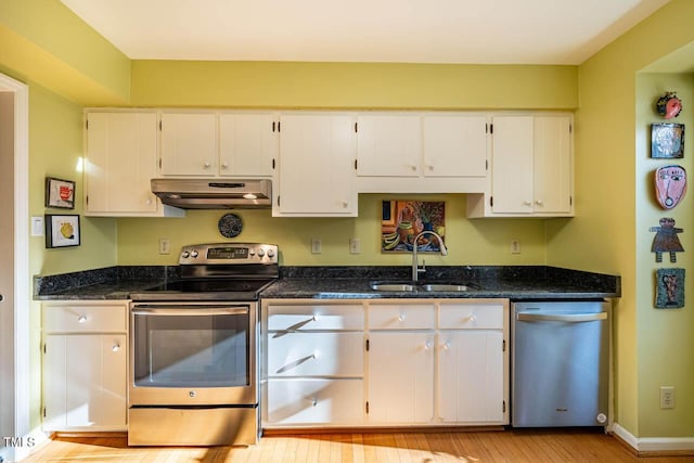 kitchen featuring light hardwood / wood-style flooring, white cabinets, appliances with stainless steel finishes, dark stone countertops, and sink