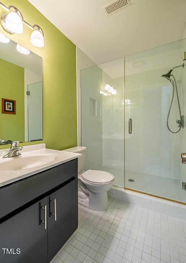 bathroom featuring toilet, tile patterned flooring, a shower with door, and vanity