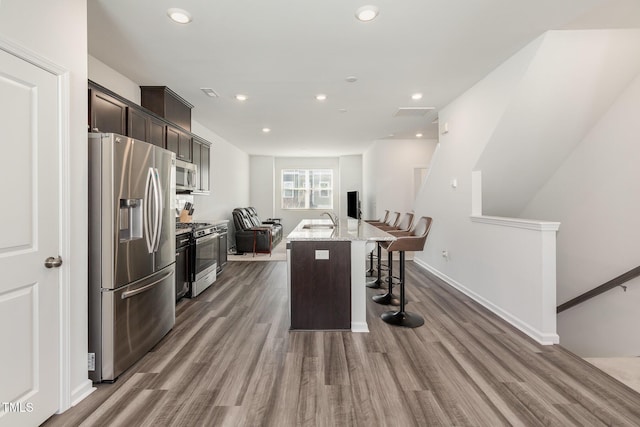 kitchen featuring light stone counters, hardwood / wood-style floors, a kitchen bar, a kitchen island with sink, and appliances with stainless steel finishes