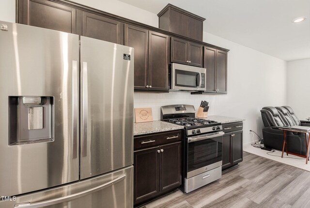 kitchen with dark brown cabinets, light stone countertops, backsplash, and appliances with stainless steel finishes