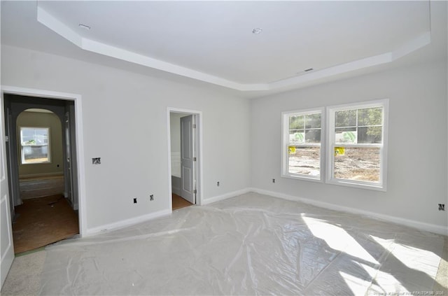 unfurnished bedroom with multiple windows and a tray ceiling