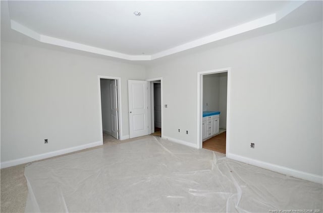 unfurnished bedroom featuring a raised ceiling, light colored carpet, and ensuite bath