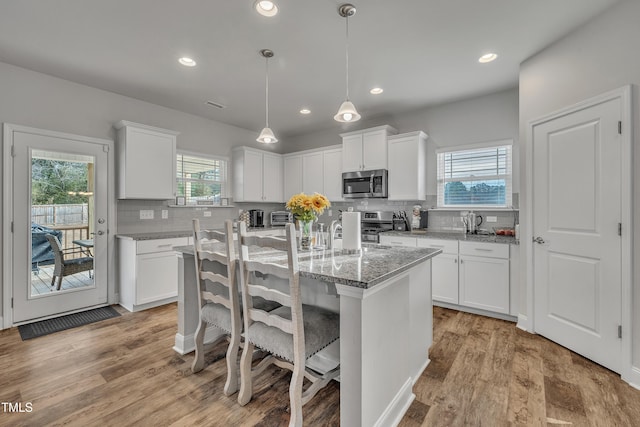 kitchen with a wealth of natural light, a kitchen island, white cabinetry, and appliances with stainless steel finishes